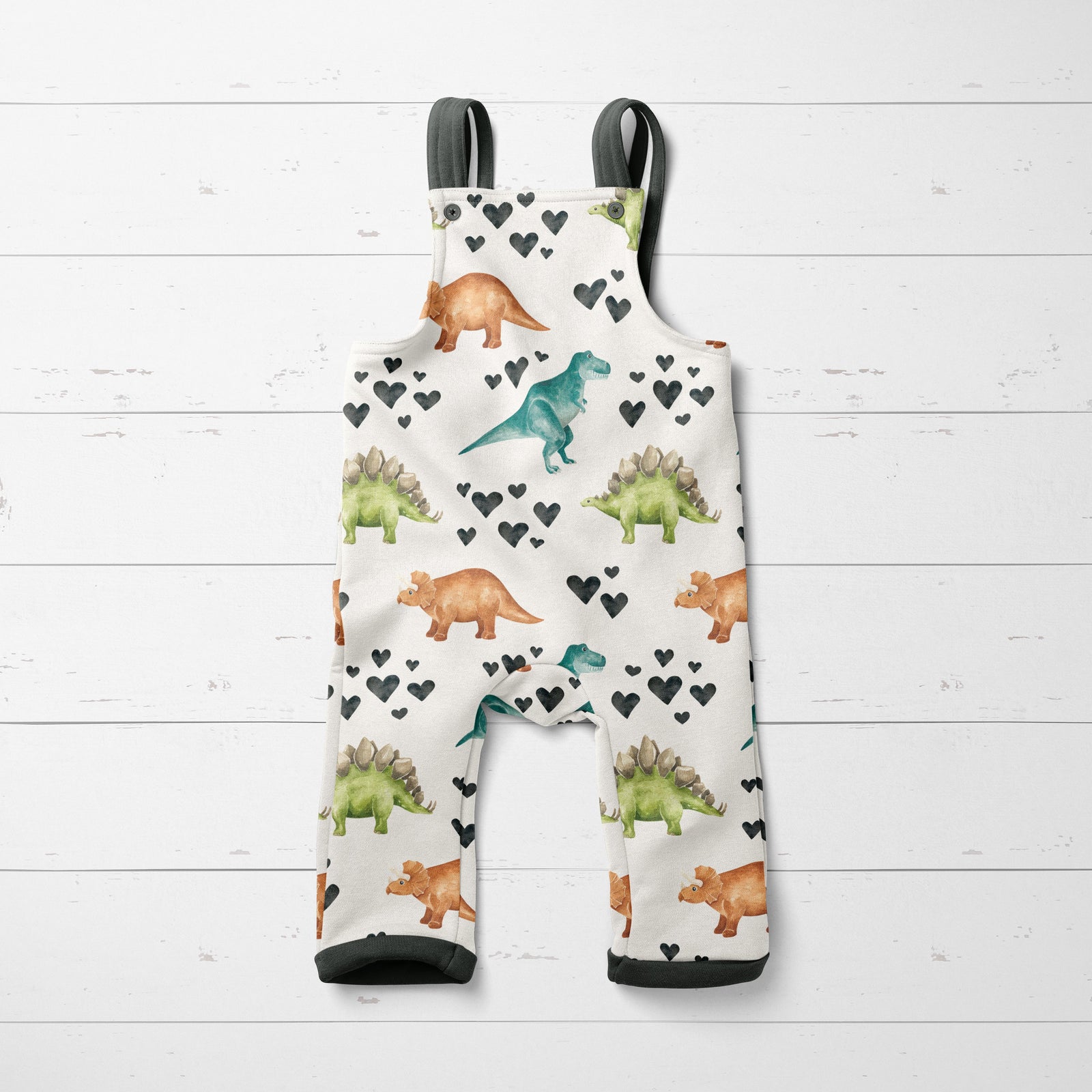 A baby outfit mockup with dinosaurs and hearts on a white wood background.